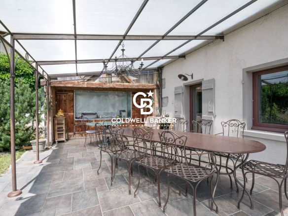 Terrasse d'une ferme rénovée avec table en fer forgé et chaises, entourée de verdure.
