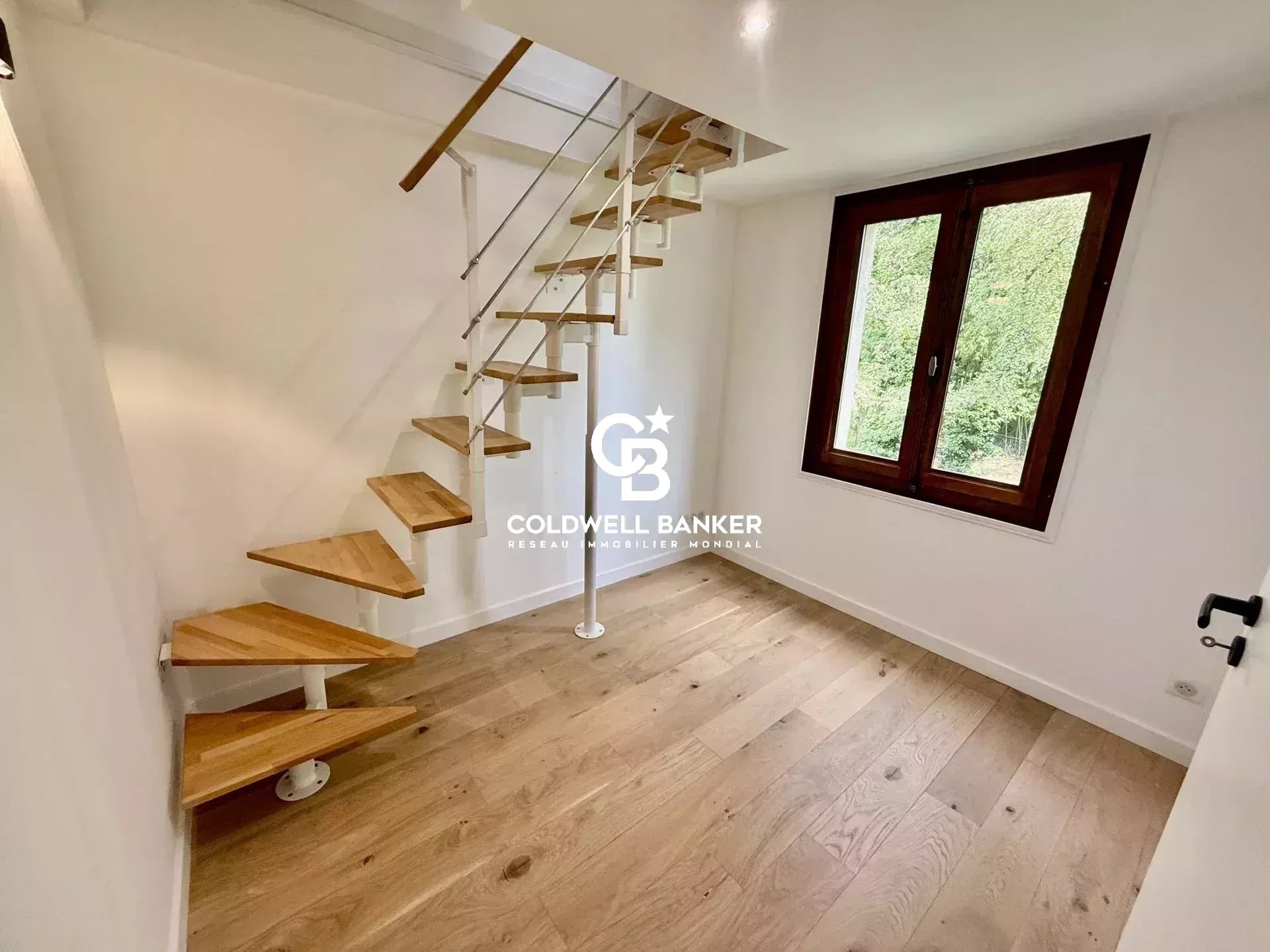 Intérieur d'une maison à vendre à Prévessin-Moëns, avec un escalier en bois et une fenêtre donnant sur l'extérieur.