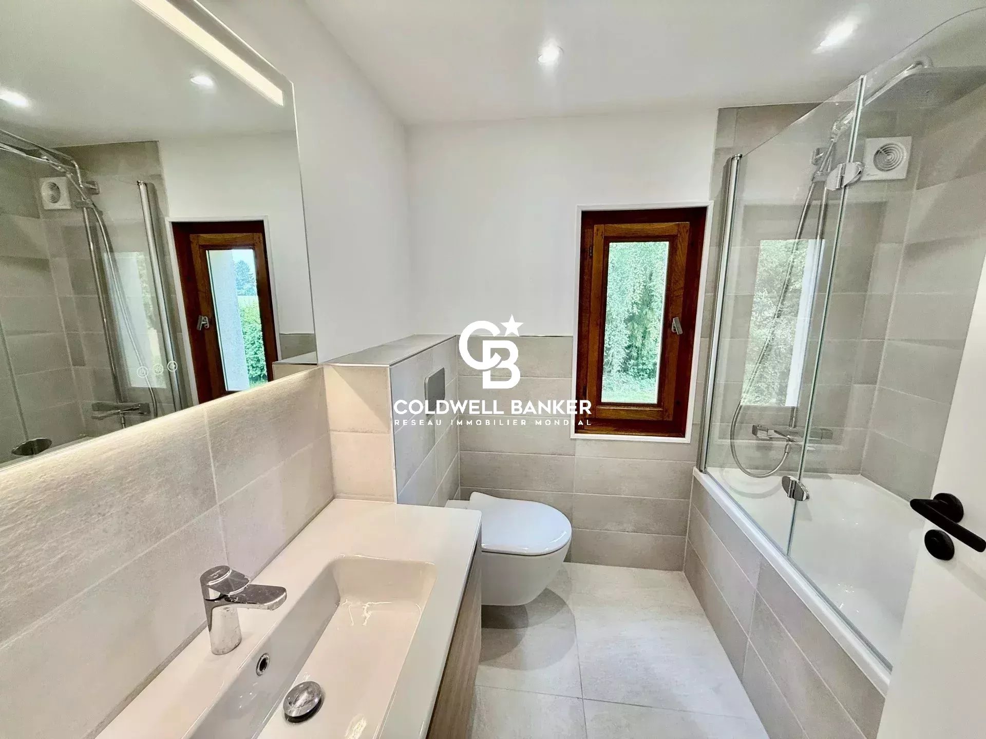 Salle de bain moderne avec baignoire et douche, fenêtres donnant sur l'extérieur.