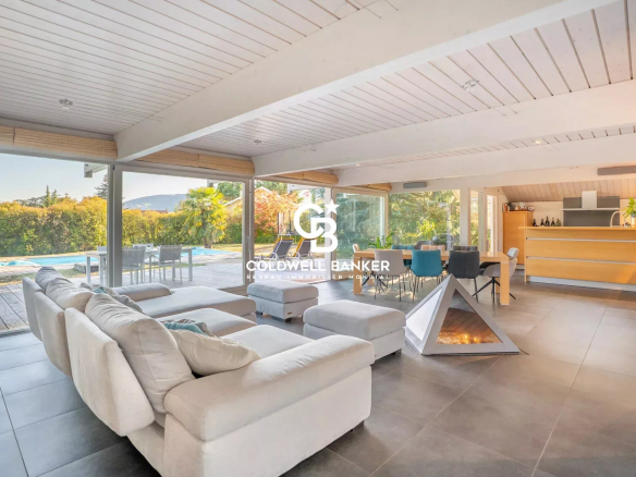 Intérieur d'une maison moderne avec salon, baies vitrées et cheminée, vue sur la piscine.