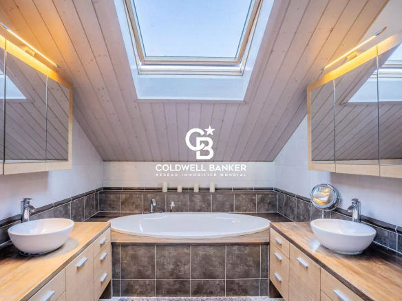 Salle de bain moderne avec baignoire et double vasque sous un toit en pente.