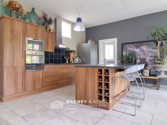 Cuisine moderne avec îlot central et bar, murs gris et éléments en bois, éclairage naturel.