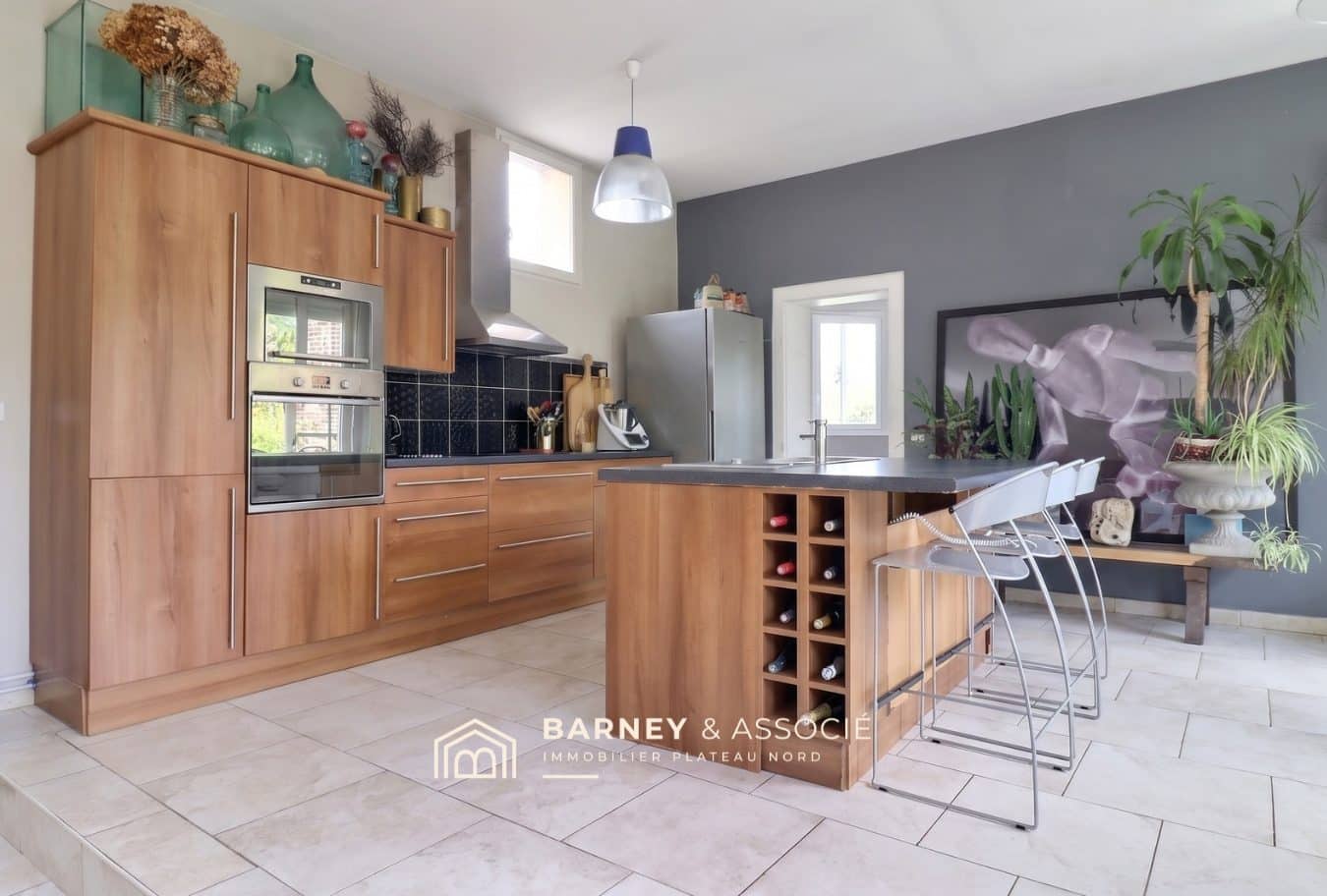 Cuisine moderne avec îlot central et bar, murs gris et éléments en bois, éclairage naturel.