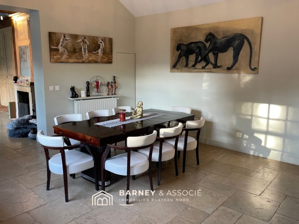 Salle à manger avec table en bois et chaises blanches, décorée de tableaux et sculptures.