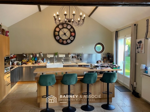 Cuisine moderne avec un grand îlot central et des tabourets, ouverte sur l'extérieur.