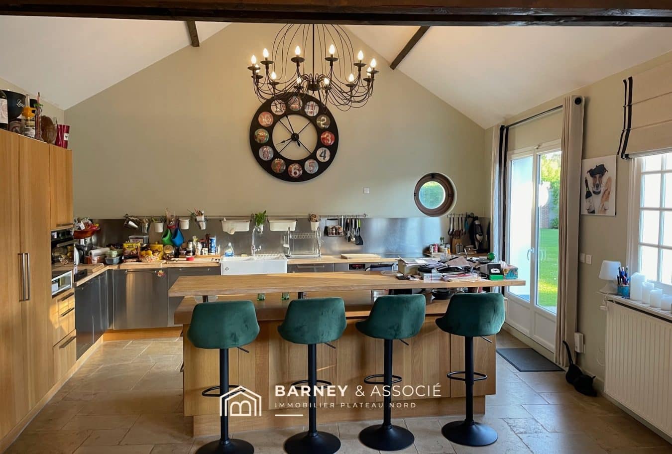 Cuisine moderne avec un grand îlot central et des tabourets, ouverte sur l'extérieur.