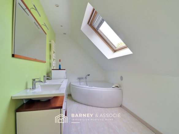 Salle de bain moderne avec baignoire et double vasque sous un plafond incliné.