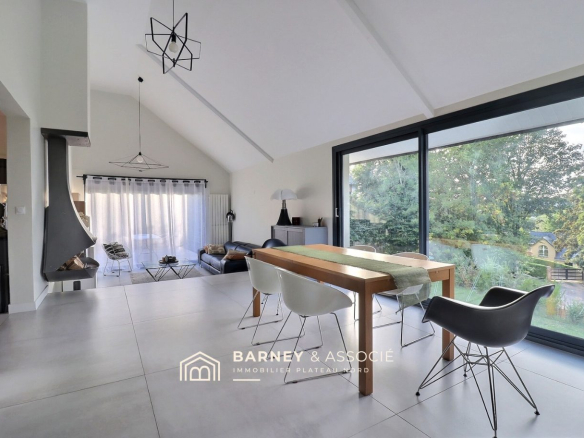 Intérieur d'une maison rénovée avec salon, salle à manger et grandes fenêtres donnant sur le jardin.