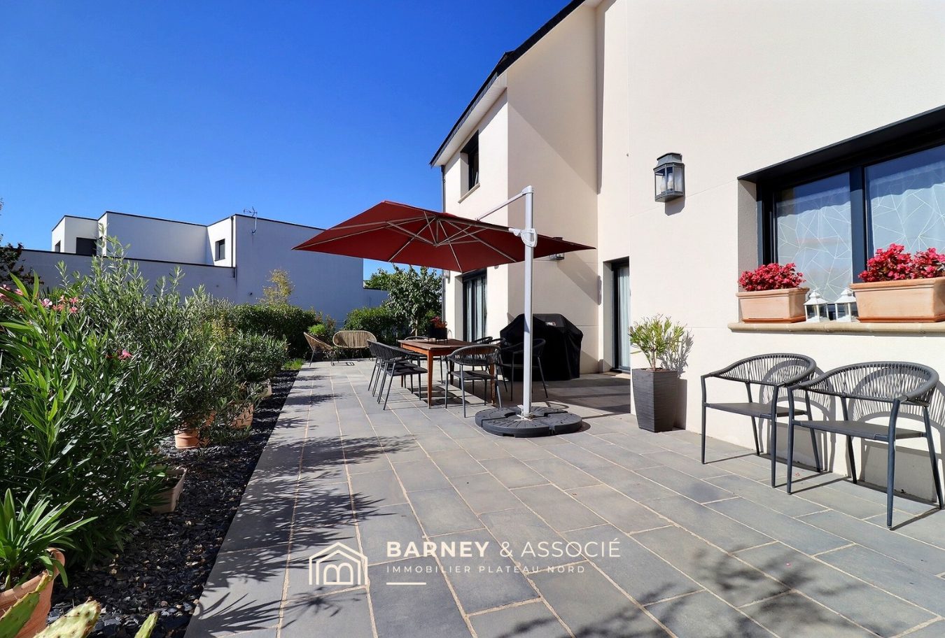 Terrasse d’une maison contemporaine à Bois-Guillaume Terrasse d'une maison contemporaine avec mobilier de jardin et parasol, entourée de verdure.