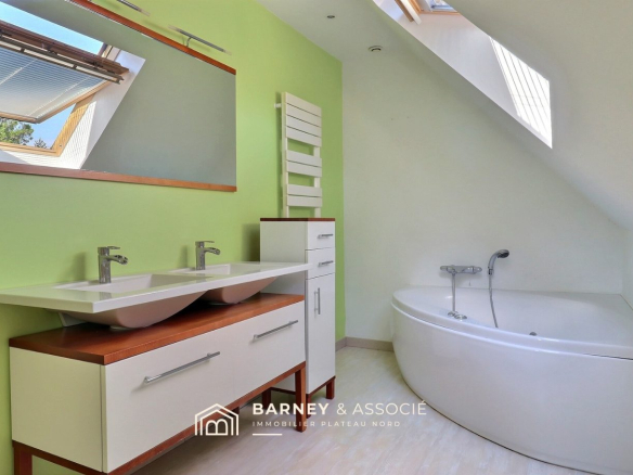 Salle de bains moderne avec double vasque et baignoire, murs verts et lumière naturelle.