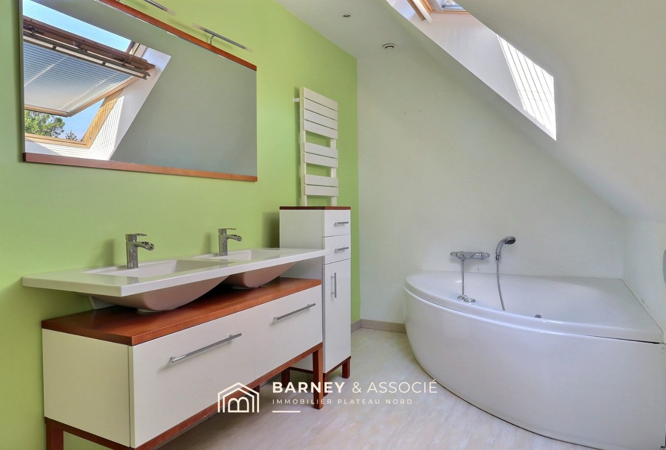 Salle de bains moderne avec double vasque et baignoire, murs verts et lumière naturelle.