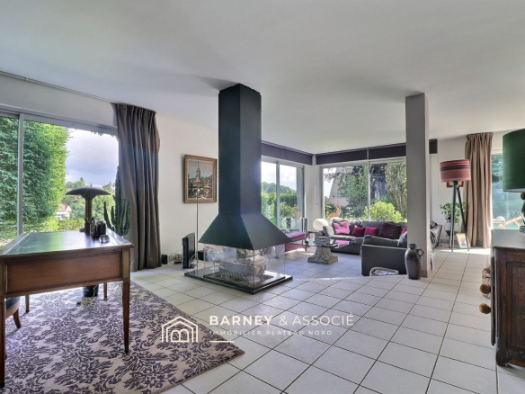 Intérieur d'une maison familiale avec salon, cheminée et fenêtres donnant sur le jardin.