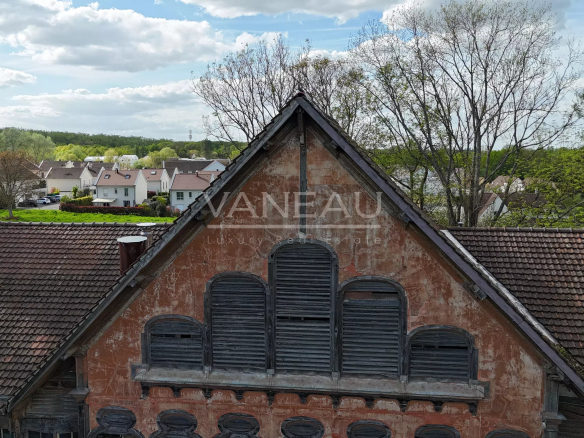 Weathered red-orange building with a steep triangular roof and arched, shuttered windows overlooking a village neighborhood.