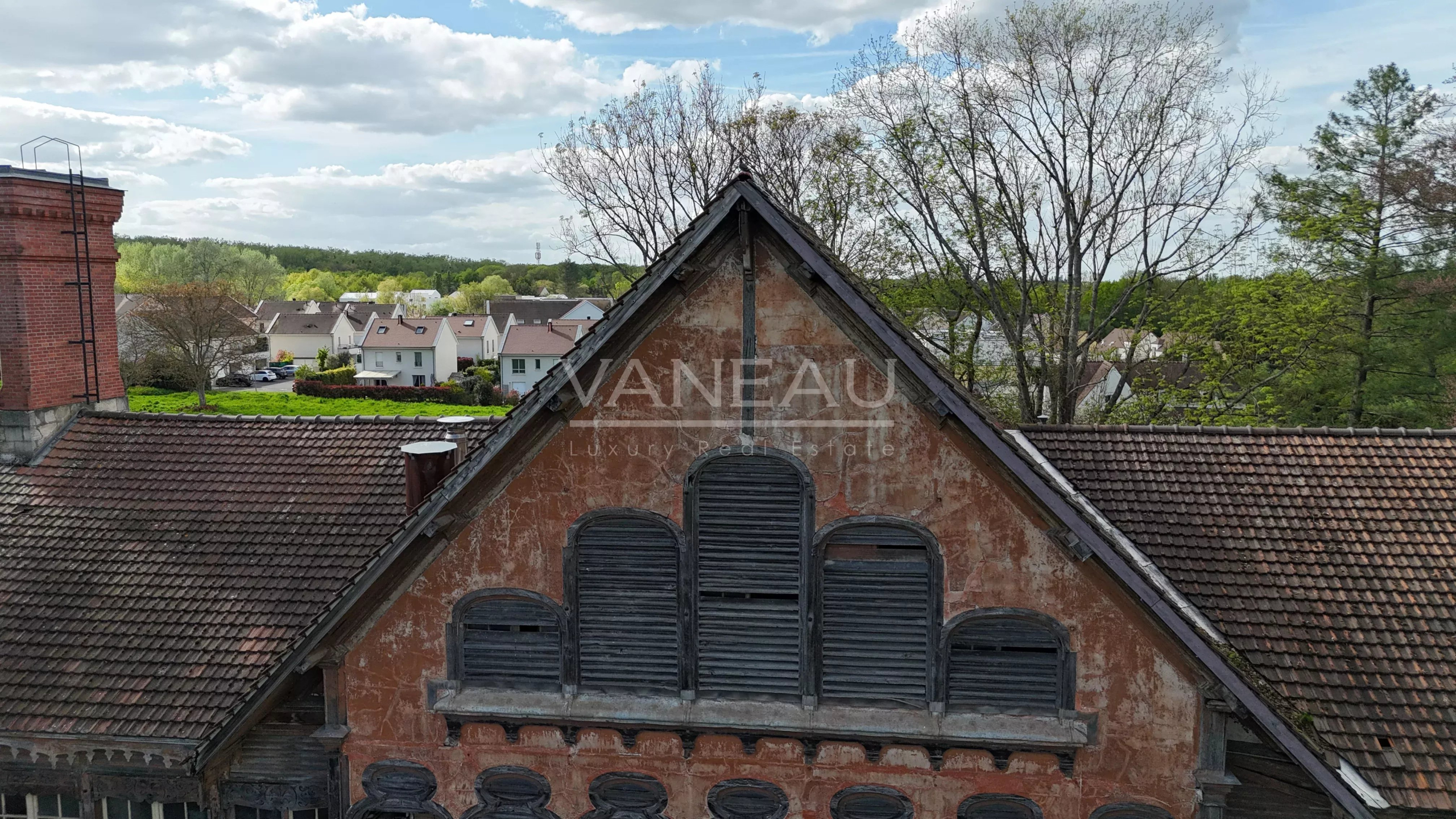 9c5b166b51a036b88f342da5f4fef5e9_96b5ee6624_4032-original Weathered red-orange building with a steep triangular roof and arched, shuttered windows overlooking a village neighborhood.