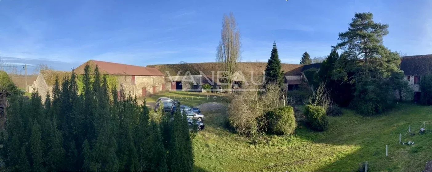 04d7f50c659371ebe709927c4fc20e19_b46d6c551f_1404-original Wide view of a rural estate with red-roofed barns, a gravel driveway, and several parked cars surrounded by tall evergreens under a clear blue sky.