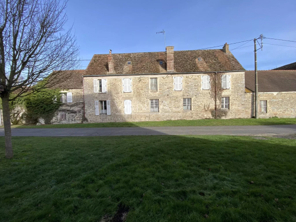 Stone two-story building with white-shuttered windows, set along a grassy foreground under a clear blue sky.