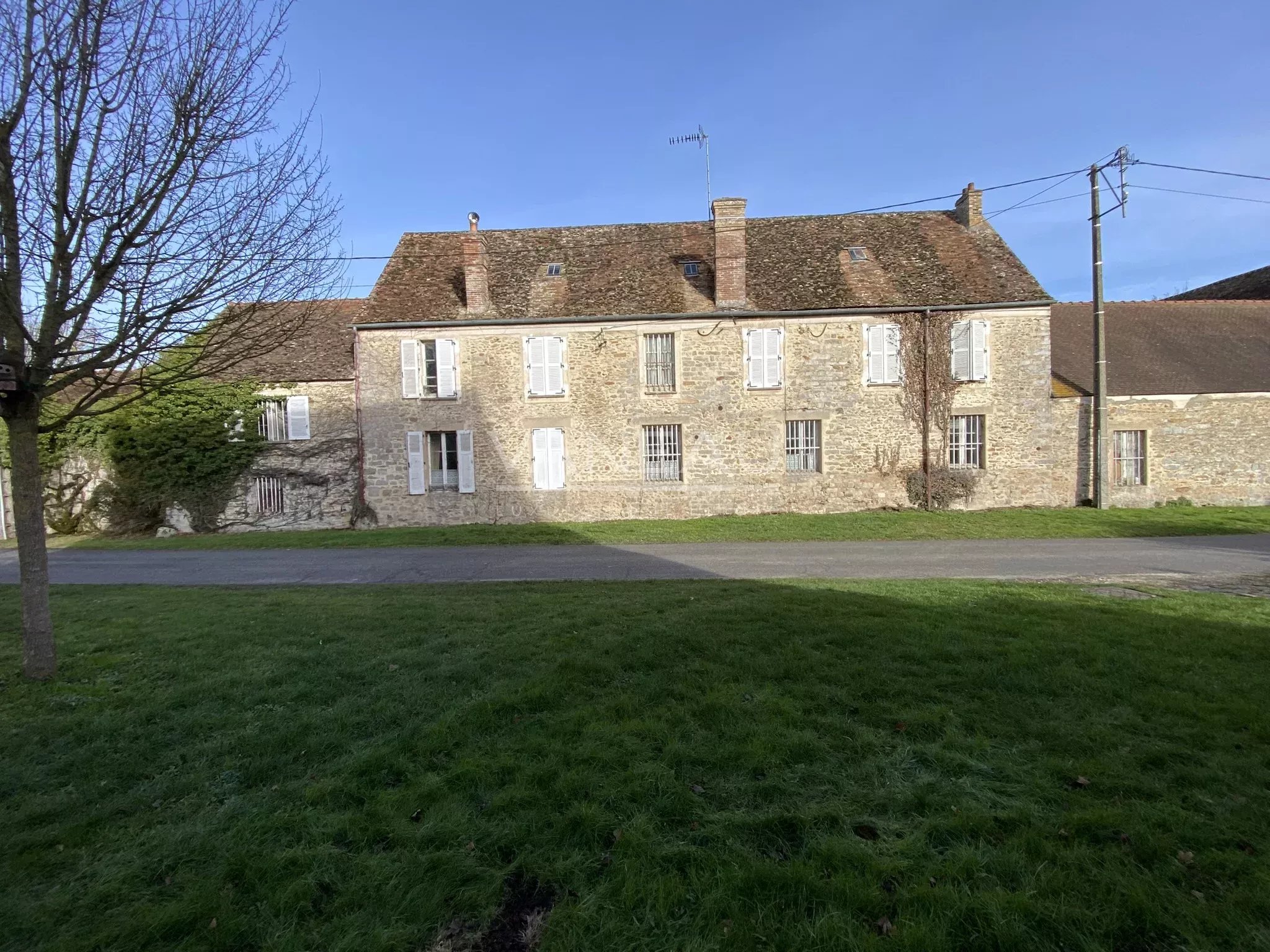 05f463bbe0d440a7c972d56b403e39d6_02a6d0cde2_2048-original Stone two-story building with white-shuttered windows, set along a grassy foreground under a clear blue sky.