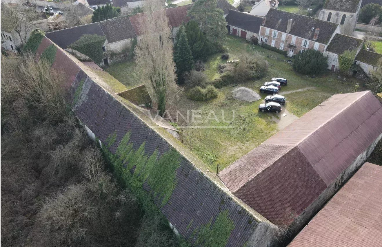 21989e49d6e49076874b001e5cfb1dec_c471248ff5_1318-original Aerial view of a historic village with steep, slate roofs, leafless trees, and a grassy yard where several cars are parked near stone buildings.