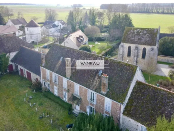 Aerial view of a quaint village: stone houses with mossy roofs, a small church, and surrounding fields.