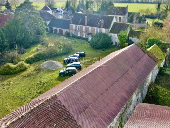 Aerial view of a village with brick houses and a long red roof, with several cars parked on a grassy yard.