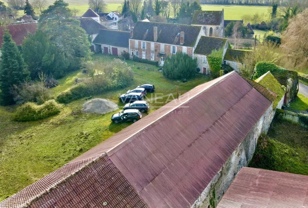 Aerial view of a village with brick houses and a long red roof, with several cars parked on a grassy yard.