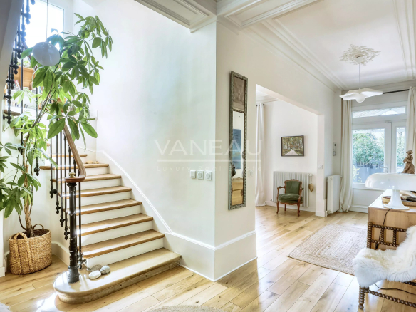 Bright foyer with curved stairway on the left, a tall potted plant, and wicker basket by the wall.