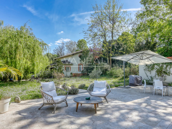 Sunny backyard patio with two wicker chairs and a round table under a large umbrella, white cushions, and a garden beyond the concrete patio.