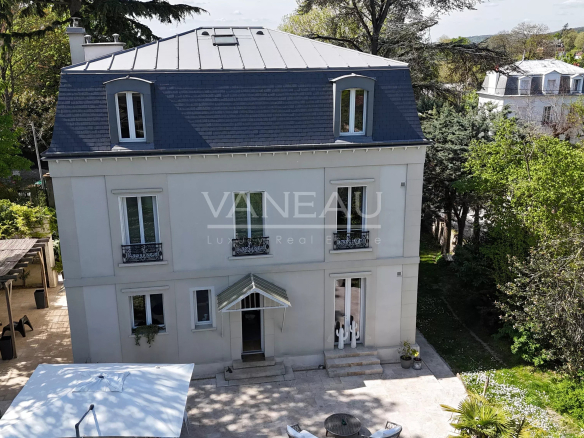 Elegant three-story house with blue mansard roof, light gray facade, and wrought-iron balcony railings viewed from above courtyard level