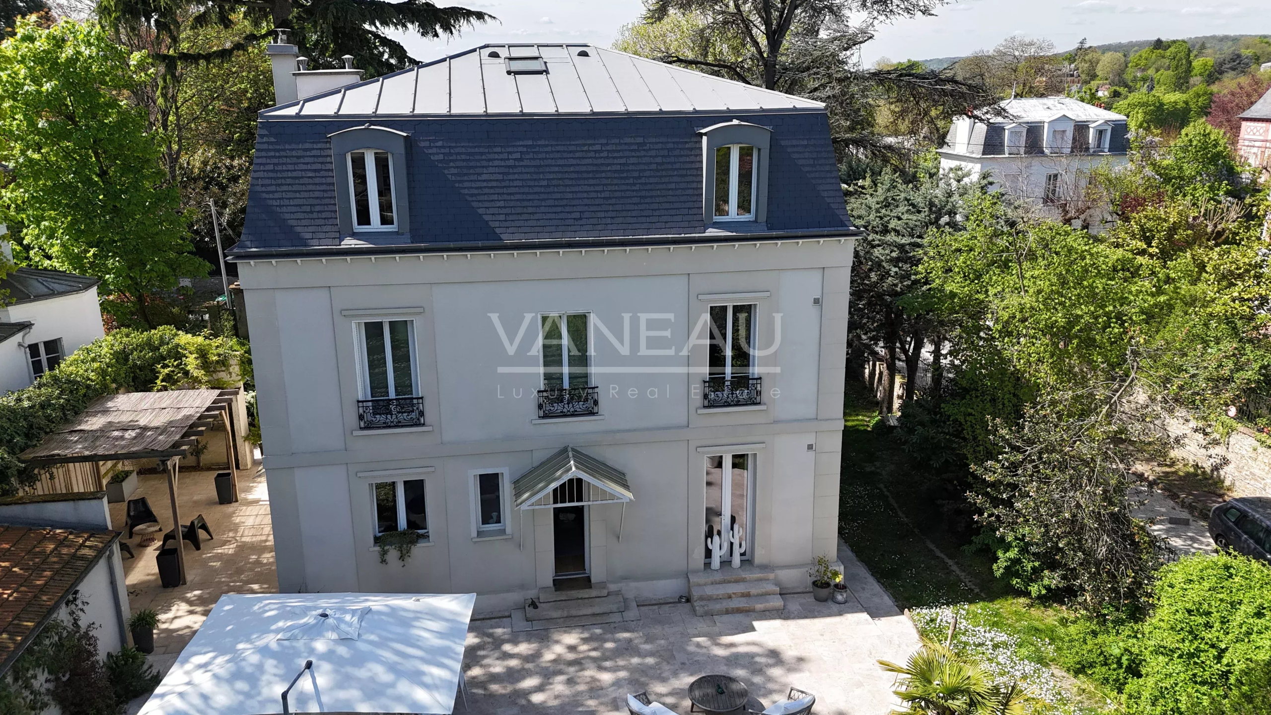 Elegant three-story house with blue mansard roof, light gray facade, and wrought-iron balcony railings viewed from above courtyard level