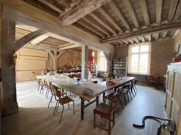 Intérieur du Manoir Henri IV avec une grande table et des chaises, éclairé par des fenêtres.