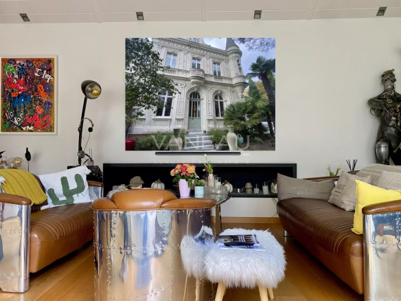 Intérieur d'un manoir rénové avec des canapés en cuir et une décoration moderne, vue sur une grande fenêtre.