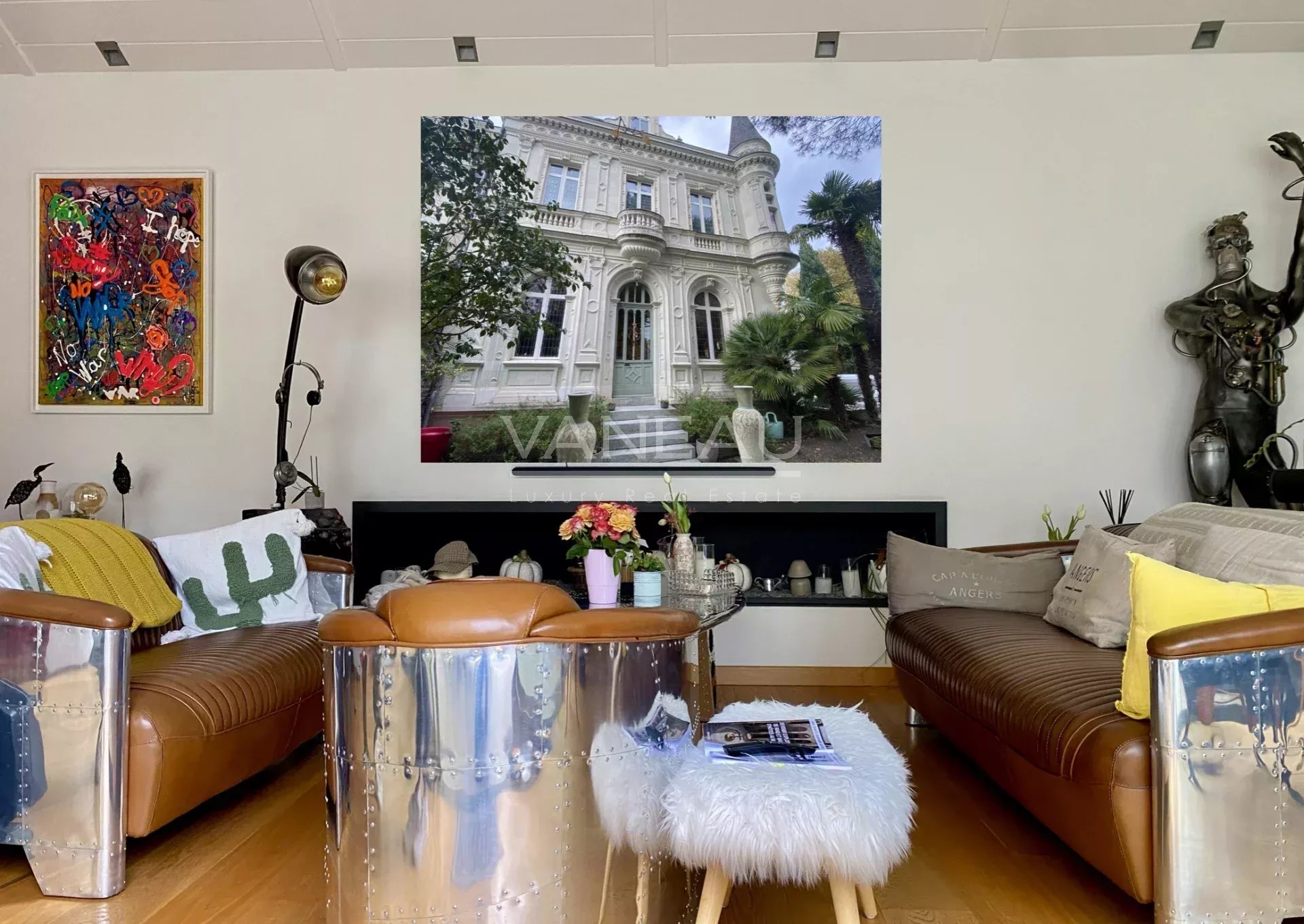 Intérieur d'un manoir rénové avec des canapés en cuir et une décoration moderne, vue sur une grande fenêtre.