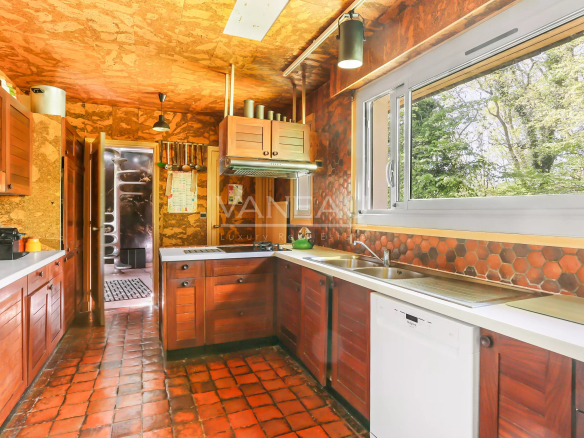 Cuisine moderne avec des meubles en bois et un plan de travail clair, fenêtres donnant sur la nature.