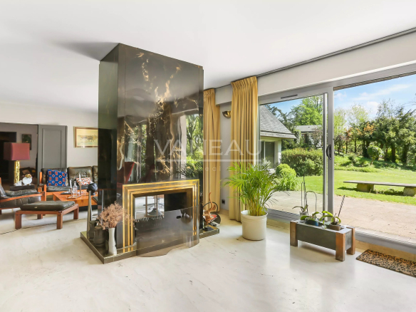 Intérieur d'une maison d'architecte moderne avec cheminée et grandes baies vitrées donnant sur le jardin.