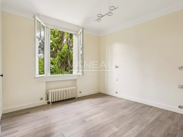 Intérieur d'une chambre lumineuse avec fenêtres ouvertes, parquet et murs clairs.