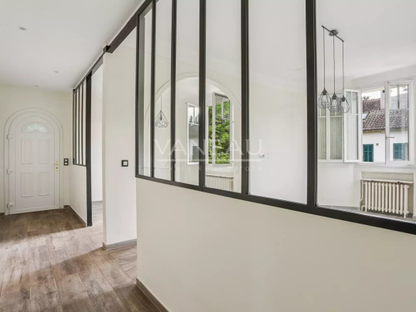 Intérieur d'une maison rénovée avec un couloir lumineux et des fenêtres en verre.