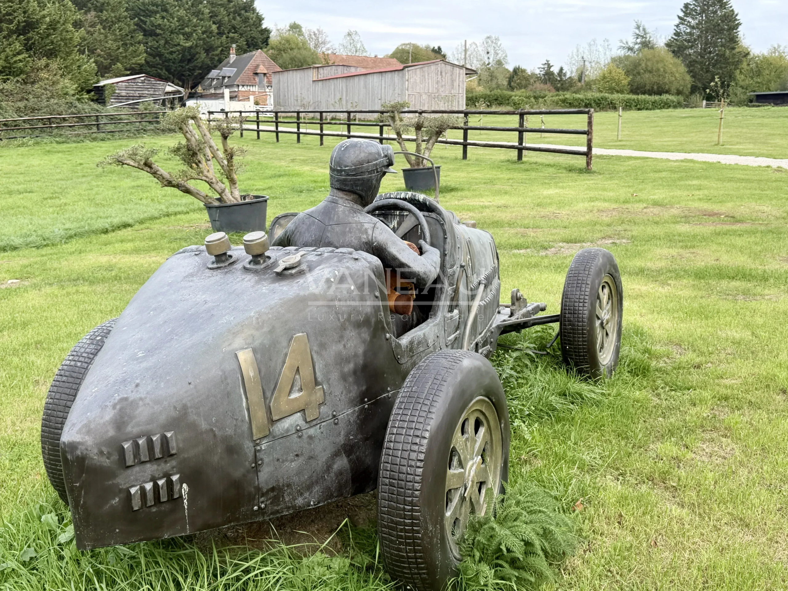 Sculpture de voiture de course Sculpture d'une voiture de course en métal avec un pilote, sur un terrain verdoyant.