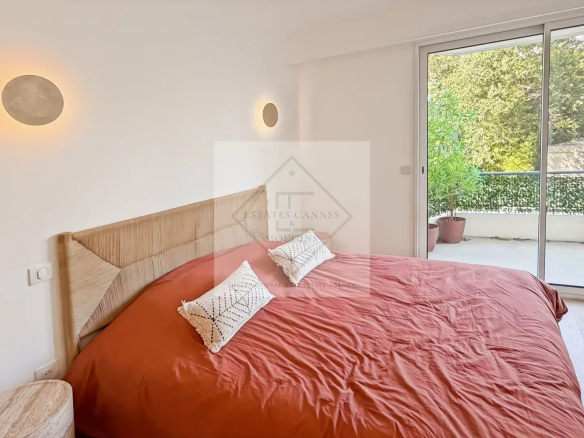 Bedroom with a rust‑orange duvet on a wooden headboard bed and a sliding glass door to a balcony outside, with potted plants visible.