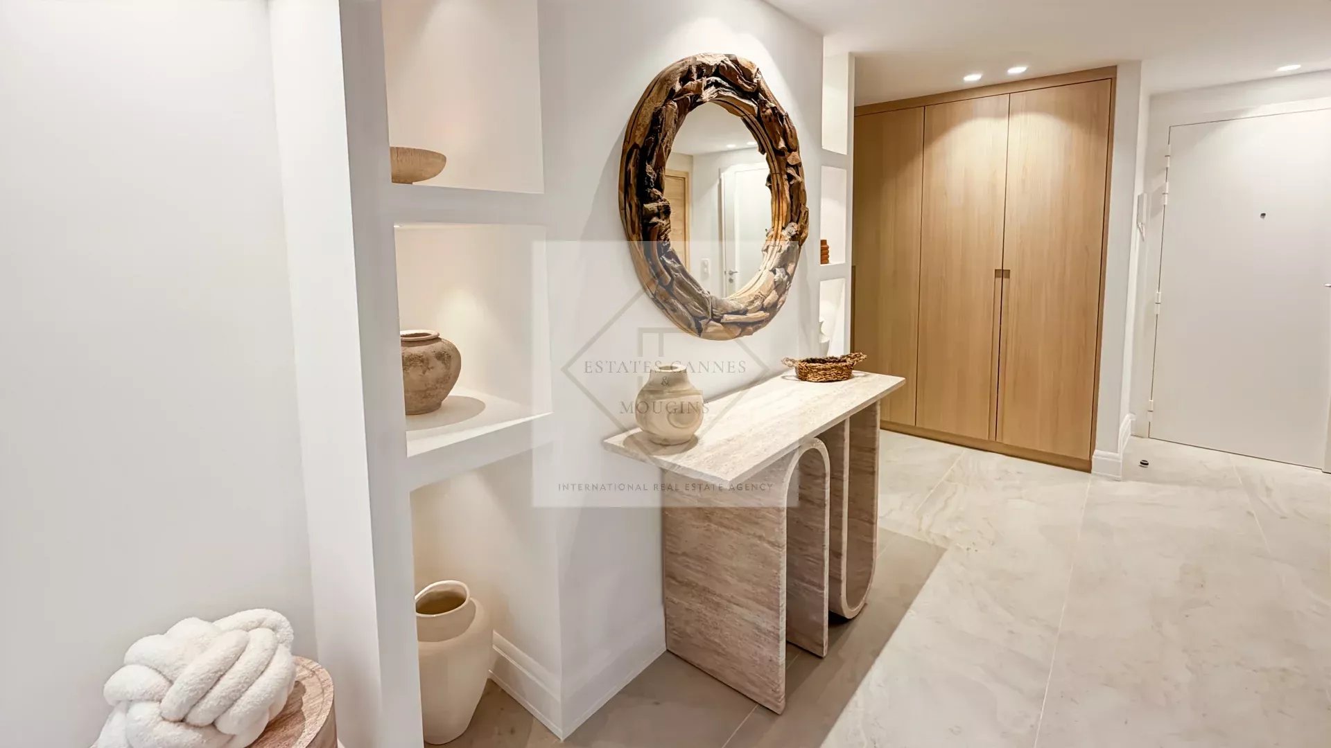 Modern foyer with a circular wooden-framed mirror above a marble console and built-in shelves displaying pottery.
