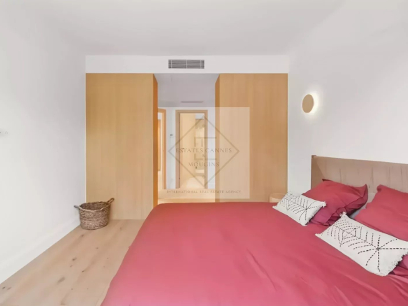 Modern bedroom featuring a red bedspread, white patterned pillows, light wood floor, and a large wooden wardrobe.