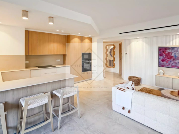 Open-concept living space with a white kitchen island, light wood cabinets, and three woven-bar stools; airy and modern.