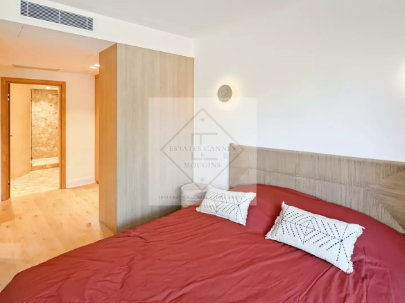 Bright bedroom with a red bedspread, white pillows, and a light wood headboard; doorway to a hallway on the left.