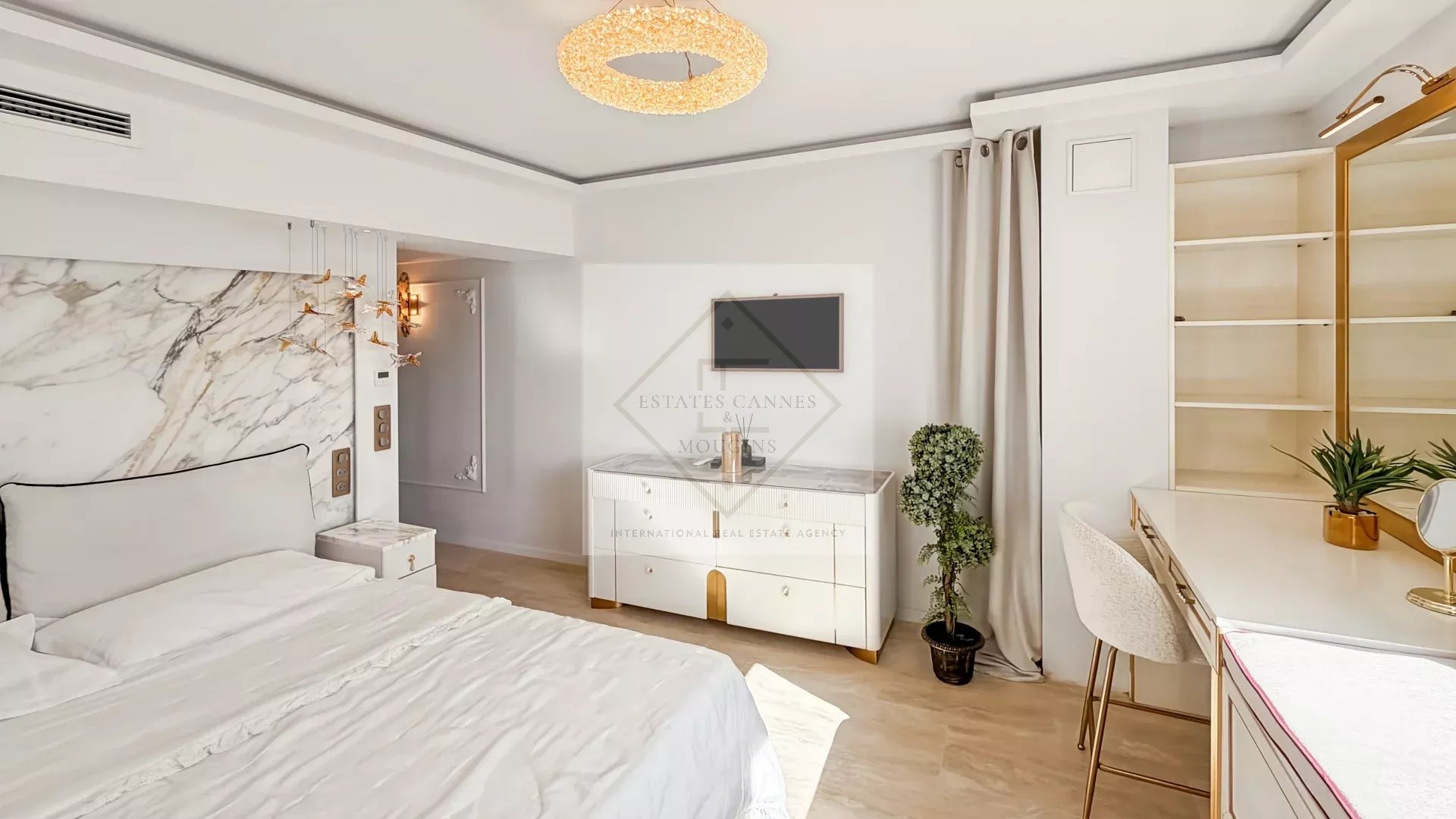 Luxurious white bedroom with marble headboard, gold accents and circular chandelier over a king bed with white bedding.