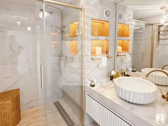 Luxurious marble bathroom with glass shower, gold fixtures, and a double sink vanity with scalloped white basins.