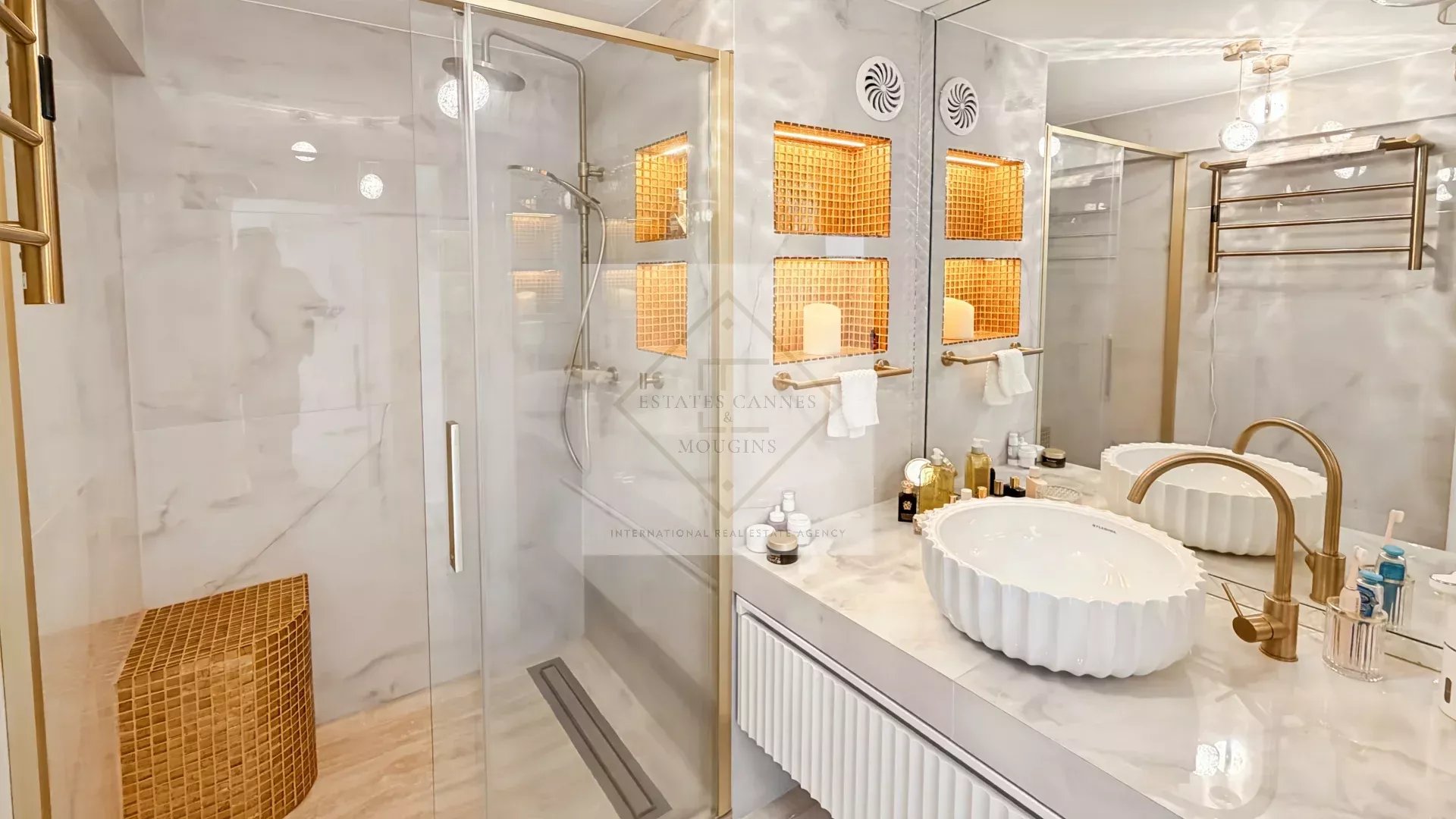 Luxurious marble bathroom with glass shower, gold fixtures, and a double sink vanity with scalloped white basins.