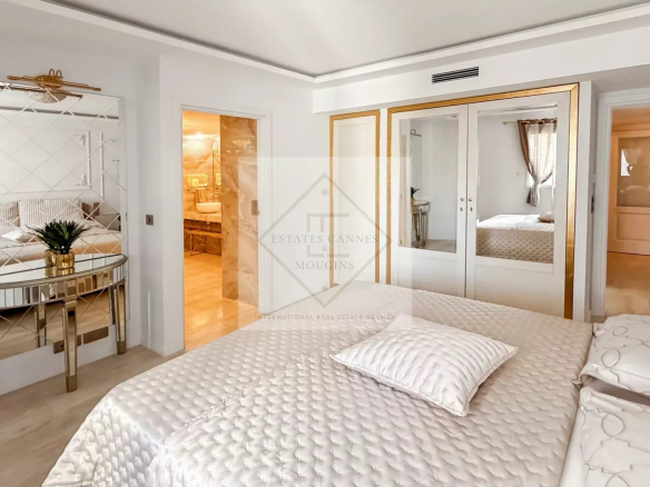 Luxurious bedroom with a white tufted bed, gold-framed mirrored wardrobe, and a glass console table with a plant.
