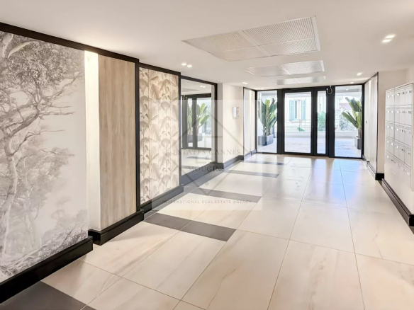 Modern residential lobby with glass entry doors, mailboxes on the right, and decorative wall panels; greenery visible outside.