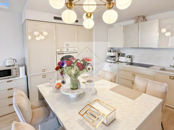 Bright white kitchen with marble island and bouquet of colorful flowers at the center dining table, brass chandelier overhead.