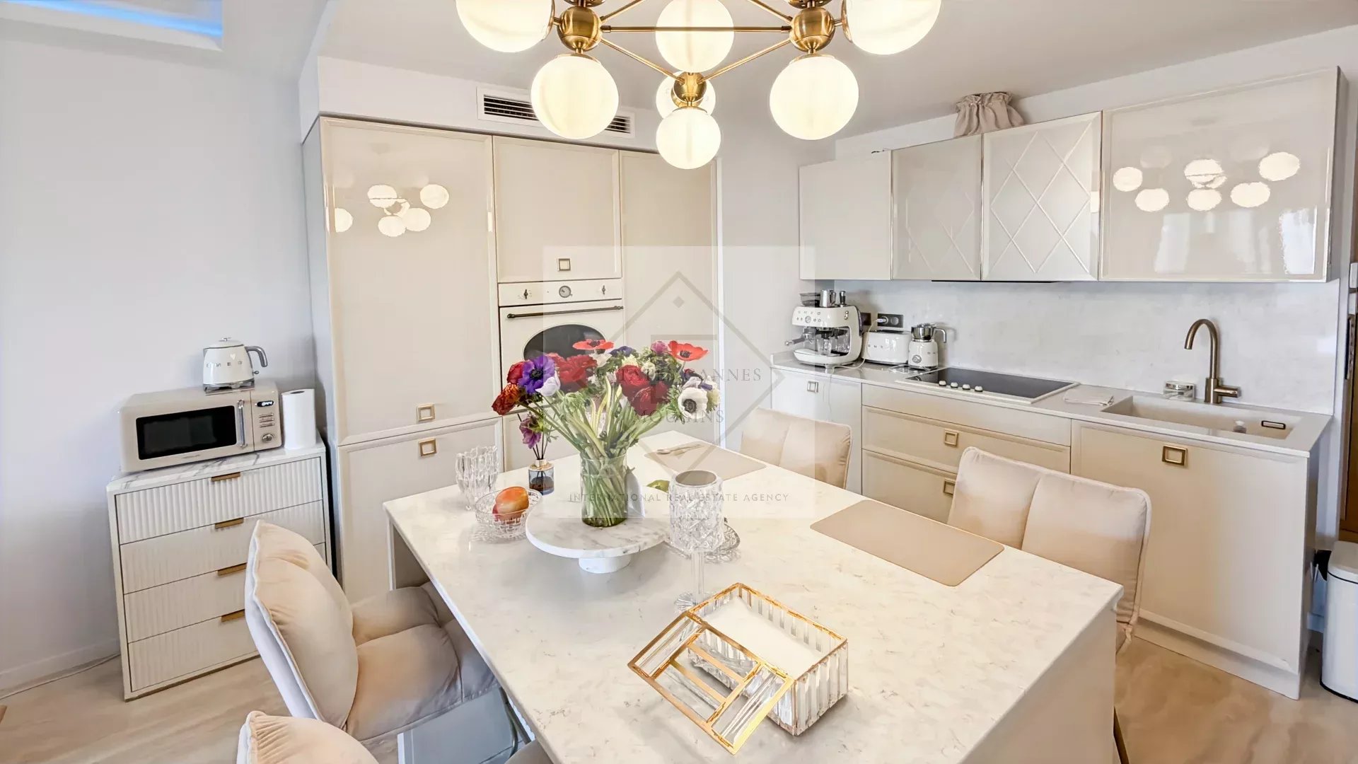 Bright white kitchen with marble island and bouquet of colorful flowers at the center dining table, brass chandelier overhead.