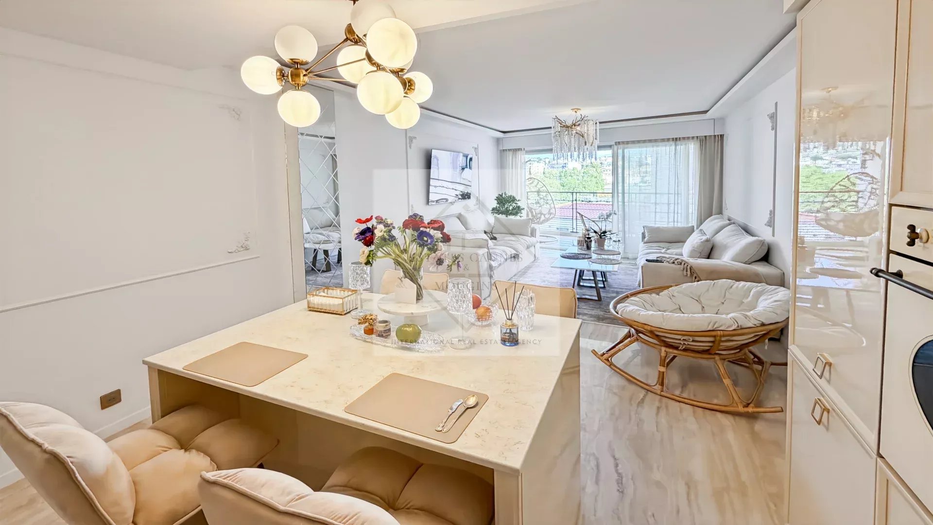 Bright open-plan kitchen and living area with a marble island, cream chairs, and a modern chandelier.